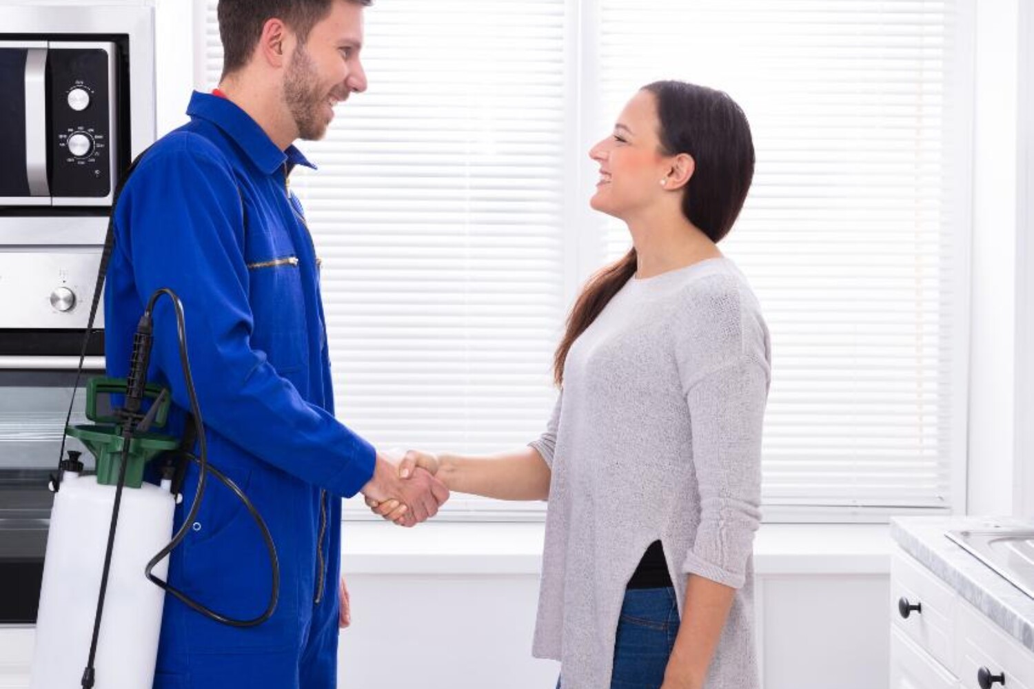 Pest control technician shaking hands with a satisfied customer in a kitchen.