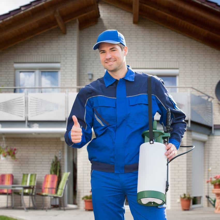 Pest control professional holding fumigation equipment in front of a house.